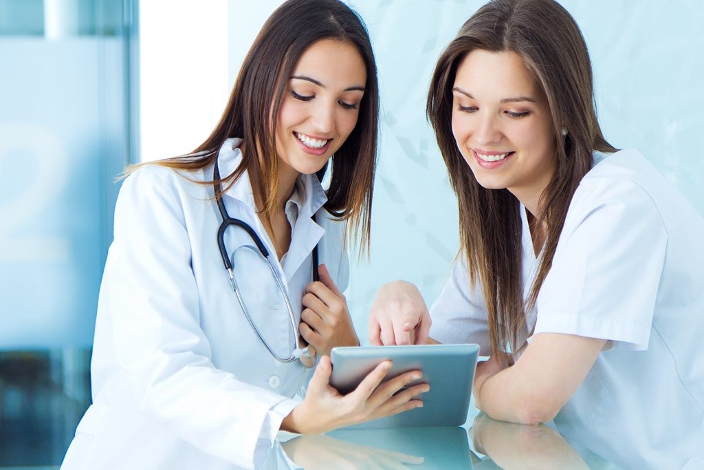Médica e enfermeira sorrindo e olhando para o tablet